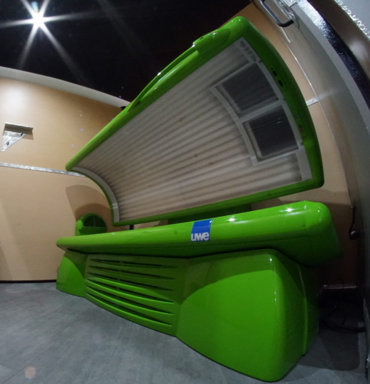 A green bench with an open tanning bed in the back.